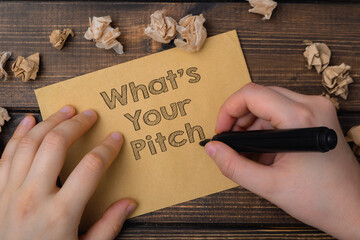 A hand is writing on a piece of paper that says What's your pitch.