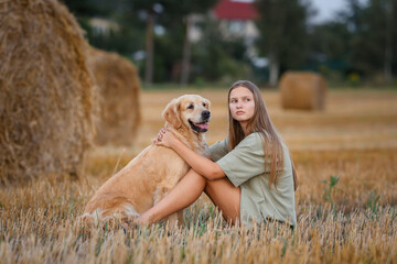 Wall Mural - beautiful girl with golden retriever dog in wheat field at sunset