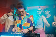 © pressmaster - Young male deejay in headphones and stylish apparel bending over soundboard while standing in front of dancing friends