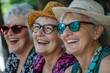 © RaptorWoman - Three joyful senior women enjoying a sunny day, laughing together while wearing stylish hats and sunglasses.