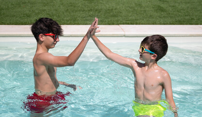 two kids high fiving as a team while enjoying in a pool. Summertime concept