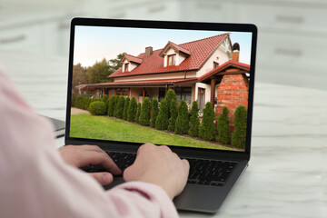 Wall Mural - Woman looking for house on real estate market website at table, closeup