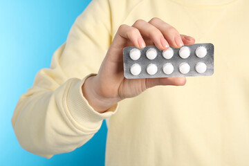 Wall Mural - Woman holding blister with antibiotic pills on light blue background, closeup