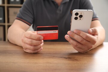 Canvas Print - Man with credit card and smartphone at wooden table indoors, closeup