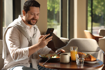 Sticker - Happy man having tasty breakfast and using smartphone in cafe