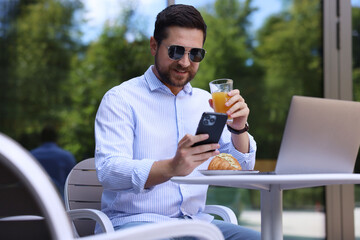 Sticker - Happy man using smartphone during breakfast in outdoor cafe