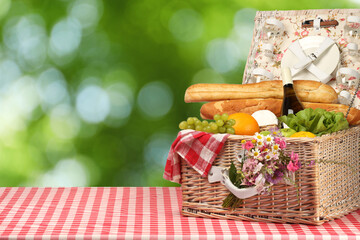 Canvas Print - Picnic basket with foods and wine on table in nature. Space for text