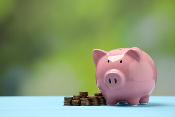 Sticker - Pink piggy bank and stacks of coins on light blue table against blurred background, space for text