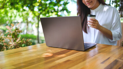 Wall Mural - Closeup image of a young woman drinking coffee and working on laptop computer in the outdoors