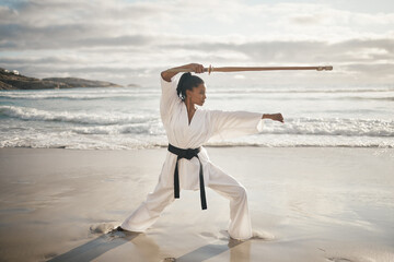 Canvas Print - Black woman, stick and beach for karate training, fitness and samurai or master fighter in outdoor. Female person, exercise and warrior for martial arts in nature, ocean and workout self defence