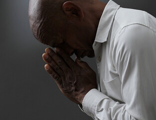 Wall Mural - man praying to god with hands together Caribbean man praying with black grey background with people stock image stock photo	