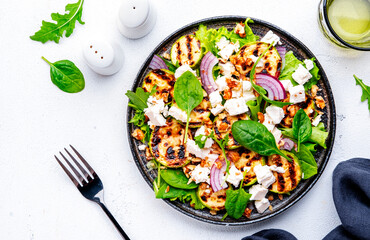 Wall Mural - Summer grill salad with zucchini, feta cheese, nuts, onion, arugula and spinach on white background, top view