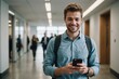 © ThomasLENNE - Portrait of Young Caucasian Man Feeling Confident as He Walks Smiling and Checking His Phone, in a Busy Office Hallway