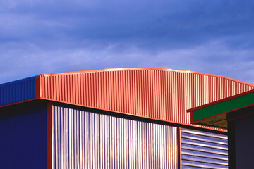 Wall Mural - Colorful warehouse building with sunlight reflection on aluminium corrugated steel wall against blue cloudy sky background in evening time, low angle and perspective side view