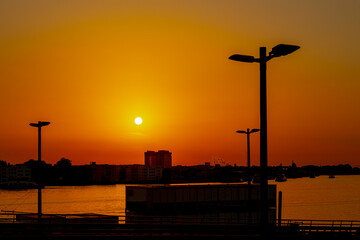 Sunrise cityscape, Silhouette of lamp post or light poles and buildings, Golden yellow sunlight and orange sky during the sun rising up in morning, Horizontal nature background, Amsterdam, Netherlands