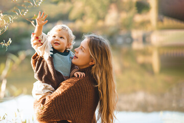 smiling happy young mother 24-26 year old holding baby girl over lake and nature background. autumn 