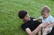 ©  Tsvyk L. - An older brother and a small child in a diaper are playing with a ball on the green grass in the yard
