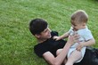©  Tsvyk L. - An older brother and a small child in a diaper are playing with a ball on the green grass in the yard