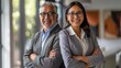 © Samady - Happy confident professional mature Latin business man and Asian business woman corporate leaders managers standing in office, two diverse colleagues executives team posing arms crossed, portrait.