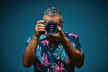 A man in studio wearing a floral shirt is taking a picture with a camera