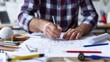 © KKC Studio - Creative Architect at Work: Sketching Blueprints at Drafting Table Surrounded by Tools and Materials for Architecture Design Process