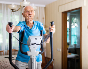 Old man using elliptic trainer at home