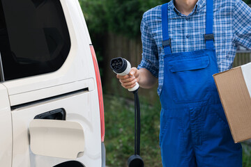 Wall Mural - Delivery man in uniform holds electric vehicle charging plug next to electric van