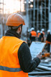 © BetterPhoto - Construction worker with orange safety vest and hard hat holding a clipboard, overseeing work at a construction site, emphasizing safety and management.