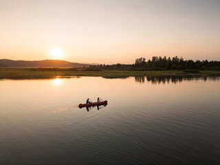 Two canoeists enjoying summer holiday activity, paddling a canoe in the tranquil lake at sunset, aerial shot. Travel and active lifestyles concept.