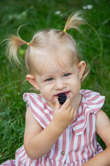 Poster - little girl eats blackberry on the background of nature. Selective focus