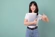 © Jirawatfoto - Technology lover concept. Cheerful asian woman pointing finger to laptop. Casual female geek hug a computer isolated on green background. Back to school concept for advertisement.