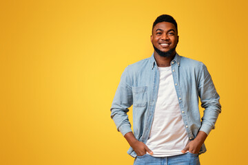 Wall Mural - Portrait of confident african american man standing with hands in pockets on yellow background with free space