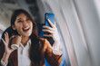 © ARMMY PICCA - .Asian woman looking at phone while sitting on airplane Technology female travelers using mobile smartphones, online apps, and the internet while sitting in airplane seats during travel.