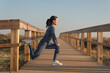© Rob Wilkinson - Sporty mid adult woman doing a leg stretch warm up exercise outdoors on a wooden boardwalk