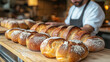 © Nataliya - A telephoto angle of bread being baked, with the loafs arranged on a wooden board and a soft focus on the baker in the background, representing the art of food preparation, with co