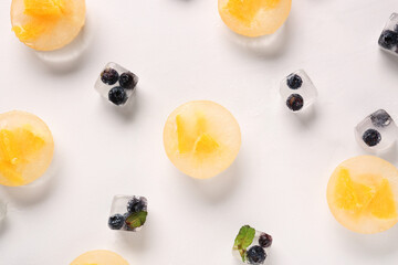 Pieces of fresh orange and blueberry frozen in ice on light background