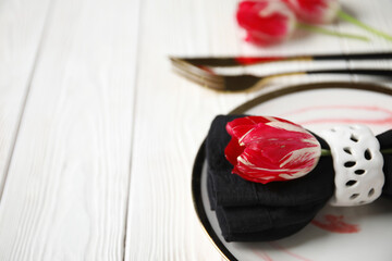 Wall Mural - Plate with folded napkin, gold cutlery and tulip flowers on white wooden background