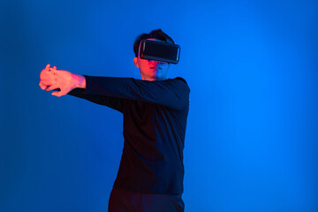 Wall Mural - Smart sportman player wearing VR stretching whole body posing on blue neon light background connecting digital futuristic technology virtual reality metaverse world in exercise concept. Contrivance.