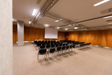 Large presentation screen in modern conference hall. Large presentation room with rows of chairs and a podium, ready for a corporate event