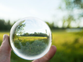 Wall Mural - glass ball in a hand and green summer nature field in the background. abstract nature background.