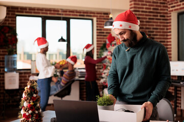 Wall Mural - Sad man in santa hat getting fired on christmas eve, packing belongings into box in decorated office. Upset disappointed company employee dismissed from job during winter holiday