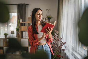 Adult young caucasian woman stand and read a book in the living room