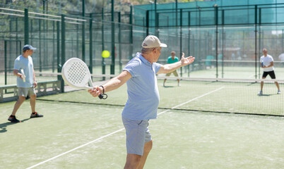 Wall Mural - Portrait of sporty senior man playing padel on open court on autumn day, ready to hit ball. Health and active lifestyle concept