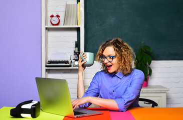 Wall Mural - Excited female teacher or university professor sitting at desk in classroom and having coffee break. Learning, education and knowledge. Surprised student or teacher in glasses at exam in college.