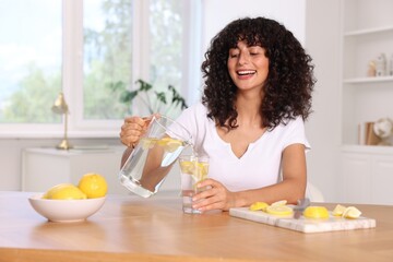 Wall Mural - Woman pouring lemon water from jug into glass at table indoors