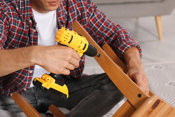 Sticker - Man repairing wooden stool with electric screwdriver indoors, closeup