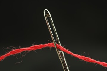 Wall Mural - Sewing needle with red thread on black background, closeup