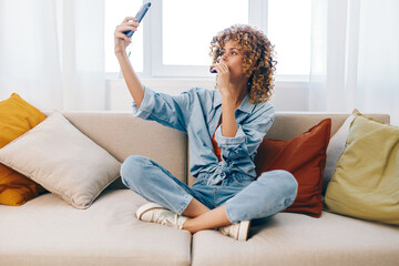 Wall Mural - Happy Woman Holding Mobile Phone, Smiling and Relaxing on Cozy Sofa in Home