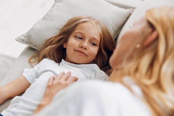 Wall Mural - Mother and daughter share a tender moment on the couch, as the little girl lies down and smiles back