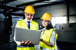 © Halfpoint - Two project managers standing in modern industrial factory, looking at laptop screen. Manufacturing facility with robotics, robotic arms and automation. Storing products and materials in warehouse.